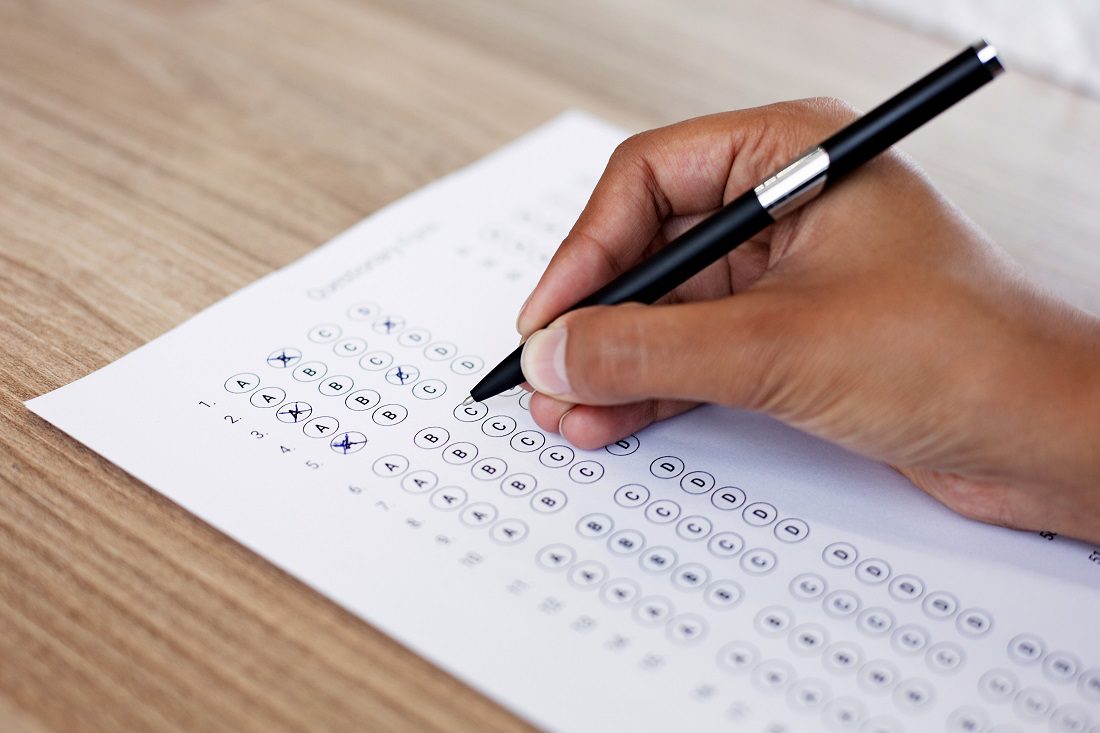 Closeup of hand holding pen and filling out questionary form on table